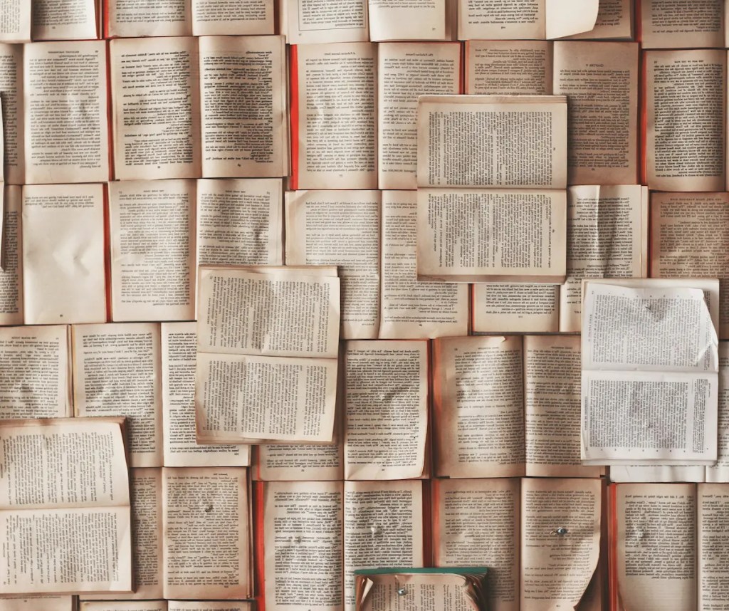Overhead view of numerous open vintage books arranged in a mosaic pattern, displaying pages of text in various fonts and layouts, creating an artistic literary collage perfect for book lovers and reading enthusiasts.